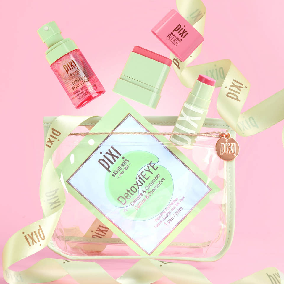 A Best of Pixi Beauty gift set arranged around a clear zip pouch on a pink background. The set includes a pink and mint detox eye cream tube, a pink and mint lip balm, a pink and mint lip product, a pink and mint cream product, and a clear pouch with a mint green border and Pixi branding. view 1